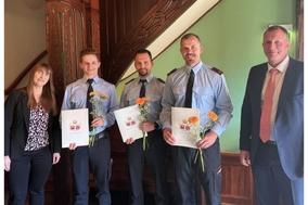 Drei Männer halten Urkunden und Blumen in den Händen, links außen steht eine Frau und rechts außen der Beigeordnete