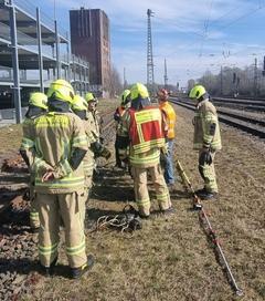 Feuerwehrmänner stehen an Bahngleisen und üben Bahnerden