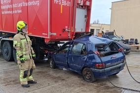 PKW unter Fahrzeug eingeklemmt, davor steht ein Feuerwehrmann