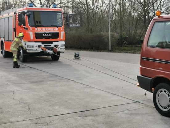 Ein Feuerwehrfahrzeug und ein MTW mit einem Feuerwehrmann. Dazwischen ist ein Seil gespannt