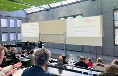 Der Hörsaal beim Netzwerktreffen von oben. Drei Leinwände, wobei nur links und rechts beschriftet ist.
