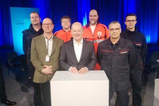 Bundeskanzler Olaf Scholz mit Vertreten der Feuerwehr und dem DRK am Rednerpult