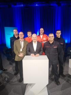 Bundeskanzler Olaf Scholz mit Vertreten der Feuerwehr und dem DRK am Rednerpult