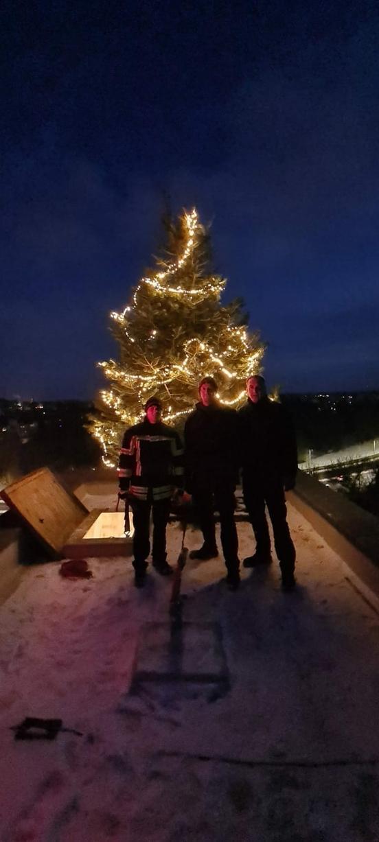 Weihnachtsbaum auf dem Schlauchturm, davor drei Feuerwehrmänner