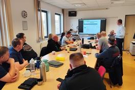 Mitarbeiter von hinten abgebildet, die im Seminarraum sitzen