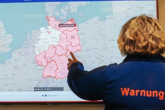 Deutschlandkarte mit rot eingefärbten Warnbereich. Davor eine Frau von hinten, die auf die Karte zeigt.