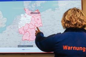 Deutschlandkarte mit rot eingefärbten Warnbereich. Davor eine Frau von hinten, die auf die Karte zeigt.