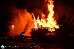 Brennende Paletten mit Flammen und einem Feuerwehrmann davor