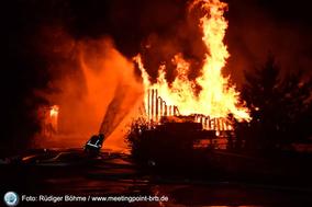 Brennende Paletten mit Flammen und einem Feuerwehrmann davor