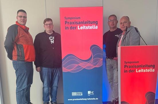 Vier Kollegen am Werbebanner zum Symposium