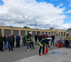 Mehrere Menschen stehen und schauen, wie eine Person mit deinem Feuerlöscher einen Brand in einer Feuerschale löscht.