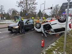 Weißer PKW liegt auf dem Dach. Ein schwarzer PKW steht daneben. Feuerwehrmänner stehen davor.