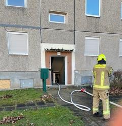 Hauseingang der offen ist. Feuerwehrmann davor mit Schläuche.