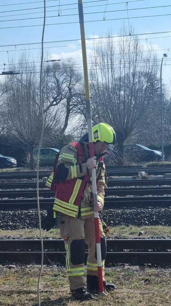 Feuerwehrmann hat eine lange Stange in der Hand, die er zu Oberleitung der Bahn führt