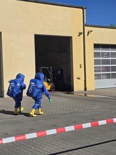 Zwei Feuerwehrmänner in blauen Schutzanzügen vor der Halle