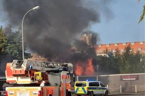 Drehleiter vor Mauer, dahinter Feuer und schwarzer Rauch.