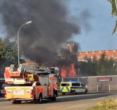 Drehleiter vor Mauer, dahinter Feuer und schwarzer Rauch.