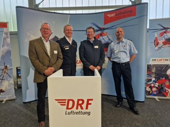 4 Männer stehen vor Werbeplakat der Deutschen Luftrettung in einer Halle