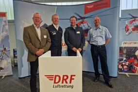 4 Männer stehen vor Werbeplakat der Deutschen Luftrettung in einer Halle