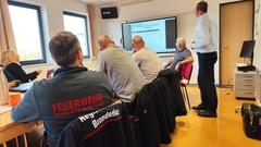 Mitarbeiter von hinten abgebildet, die im Seminarraum sitzen