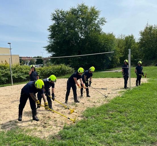 Feuerwehrmänner auf Sandfläche mit Handwerksgerät in den Händen