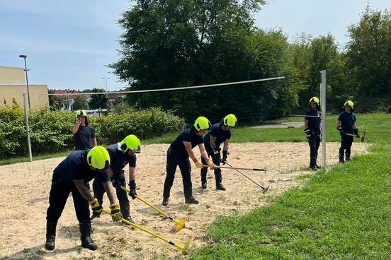 Feuerwehrmänner auf Sandfläche mit Handwerksgerät in den Händen