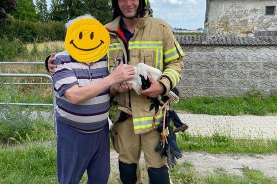 Feuerwehrmann mit einem älteren Herrn und einem Storch im Arm