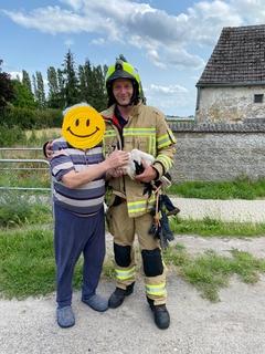 Feuerwehrmann mit einem älteren Herrn und einem Storch im Arm