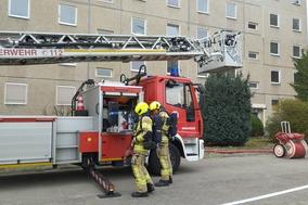 2 Feuerwehrmänner vor der Drehleiter. Sie setzen gerade die PA Flaschen auf.