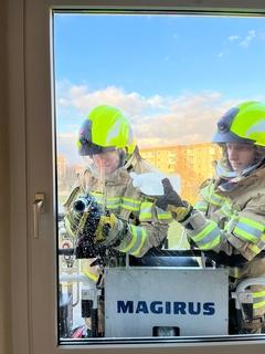 Zwei Feuerwehrleute am Fenster. Eine fräst ein Loch in die Scheibe.