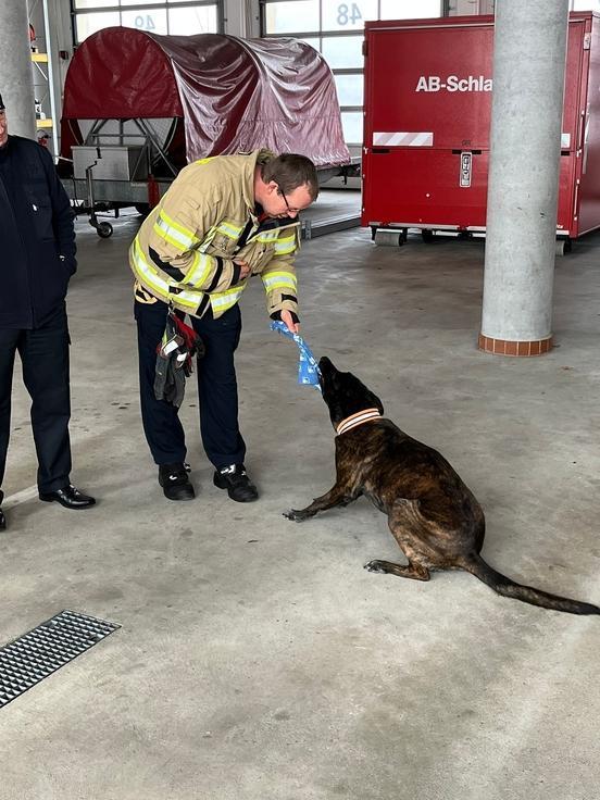 Ein Feuerwehrmann spielt mit einem Hund in der Fahrzeughalle.