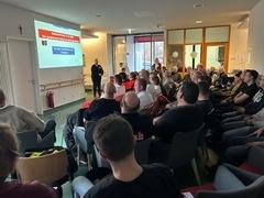 Sitzende Menschen in einem großen Raum mit Leinwand