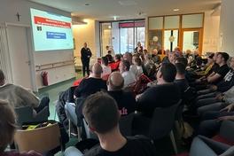 Sitzende Menschen in einem großen Raum mit Leinwand